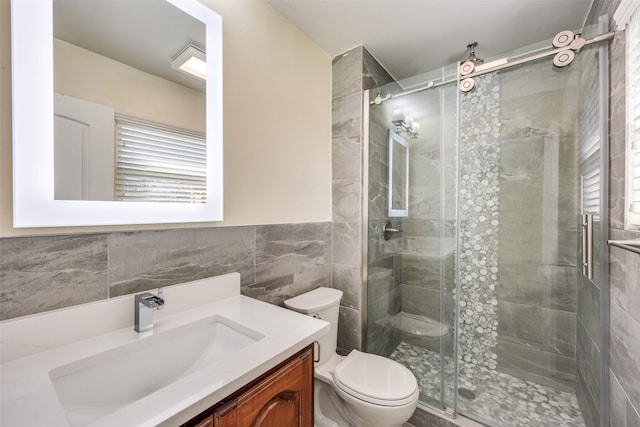 bathroom with vanity, toilet, a shower with shower door, and tile walls