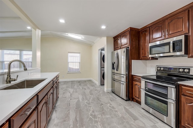 kitchen with vaulted ceiling, appliances with stainless steel finishes, sink, stacked washer and clothes dryer, and crown molding