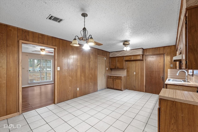 kitchen featuring light tile patterned flooring, sink, a textured ceiling, and wooden walls