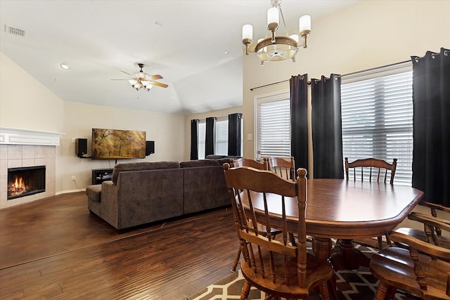 dining area featuring lofted ceiling, ceiling fan with notable chandelier, dark hardwood / wood-style flooring, and a tile fireplace