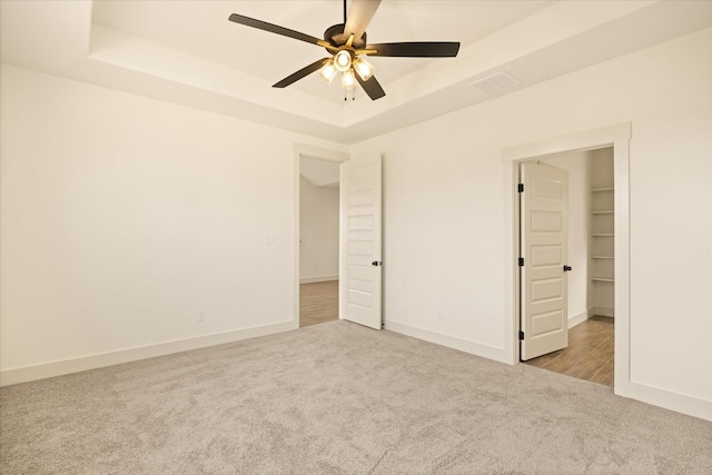 unfurnished bedroom featuring ceiling fan, light colored carpet, a tray ceiling, and a spacious closet