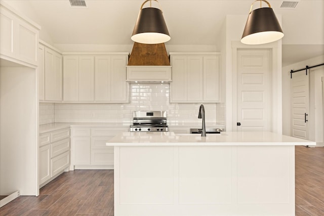 kitchen featuring pendant lighting, stainless steel range, a barn door, and an island with sink