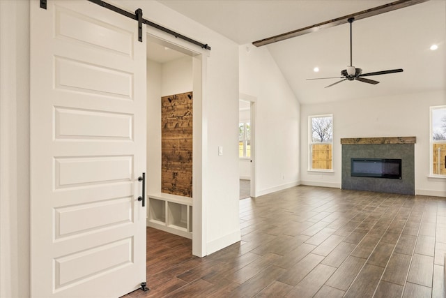 unfurnished living room featuring dark wood-type flooring, ceiling fan, a barn door, and vaulted ceiling