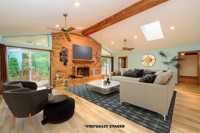 living room featuring lofted ceiling with skylight, a brick fireplace, ceiling fan, and light hardwood / wood-style floors