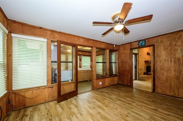 empty room with ceiling fan, ornamental molding, wooden walls, and light wood-type flooring