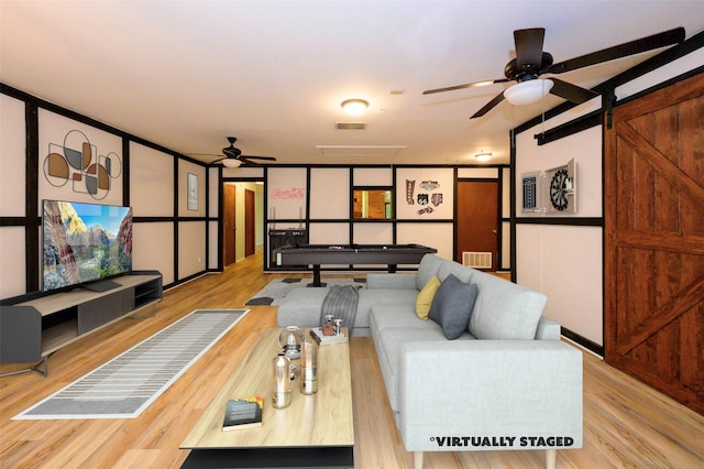 living room with ceiling fan, a barn door, and light wood-type flooring