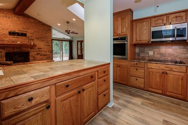 kitchen featuring appliances with stainless steel finishes, backsplash, light hardwood / wood-style floors, a brick fireplace, and tile countertops