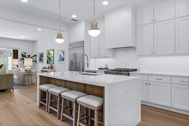 kitchen featuring sink, stove, white cabinets, a center island with sink, and built in fridge