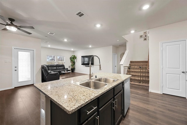 kitchen with sink, a kitchen island with sink, light stone countertops, dark hardwood / wood-style flooring, and stainless steel dishwasher