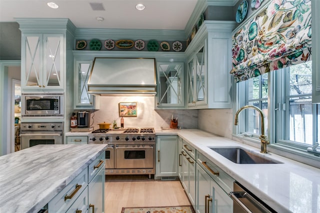 kitchen with sink, light stone counters, custom range hood, stainless steel appliances, and backsplash