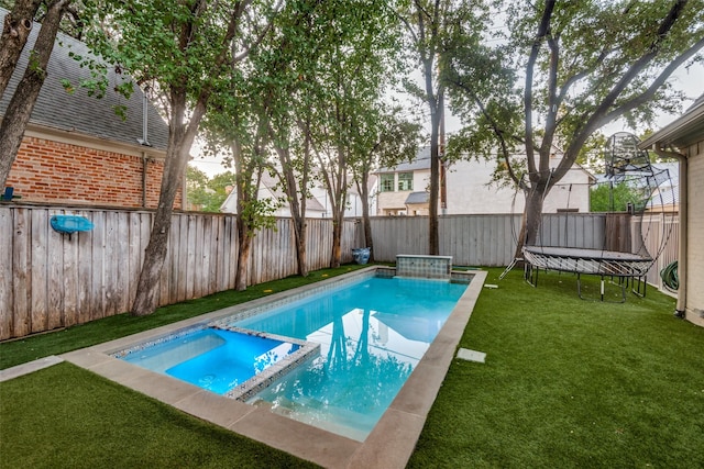 view of pool with an in ground hot tub, a yard, and a trampoline