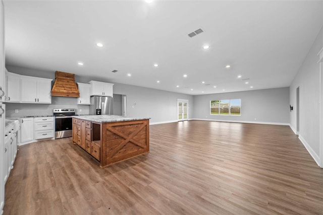 kitchen featuring appliances with stainless steel finishes, white cabinetry, a center island, light stone countertops, and custom exhaust hood