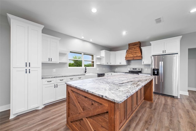 kitchen featuring white cabinetry, stainless steel appliances, a center island, light stone counters, and custom range hood