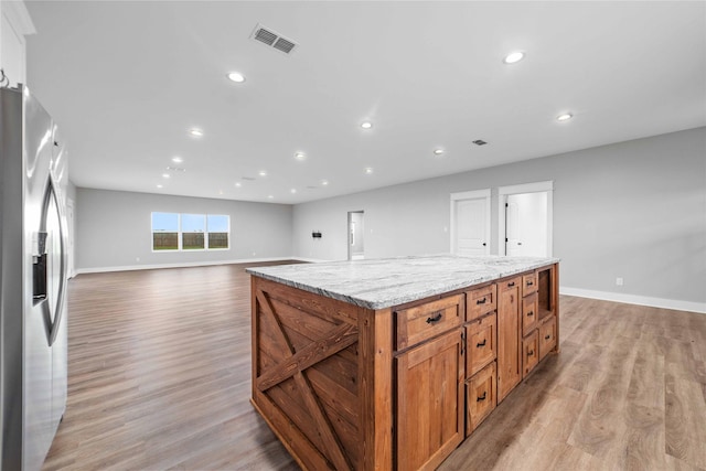 kitchen featuring light hardwood / wood-style floors, light stone countertops, stainless steel fridge with ice dispenser, and a kitchen island