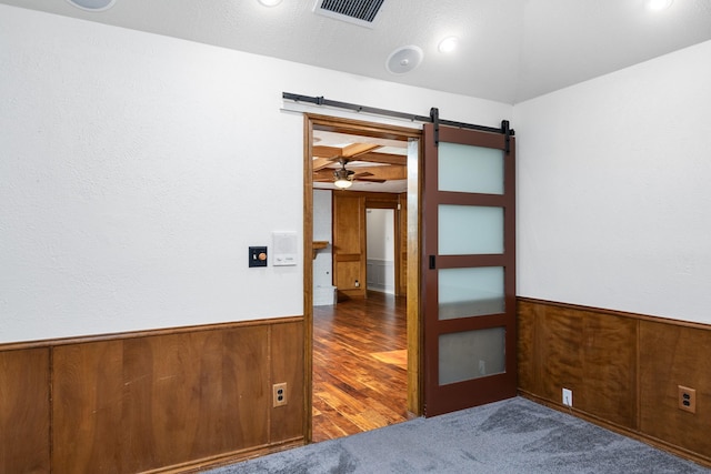 empty room with dark wood-type flooring, a barn door, and wood walls