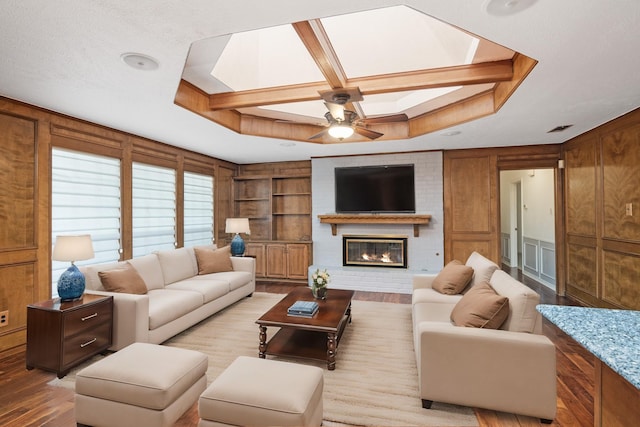 living room featuring coffered ceiling, a brick fireplace, built in features, and light wood-type flooring