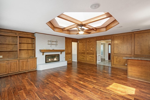 unfurnished living room with dark hardwood / wood-style flooring, ceiling fan, a fireplace, and a skylight