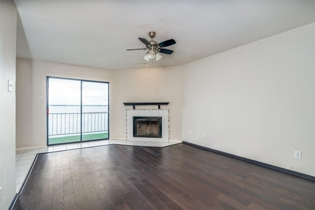 unfurnished living room with wood-type flooring, a ceiling fan, a tile fireplace, and baseboards