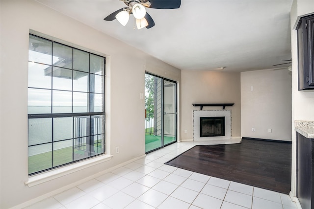 unfurnished living room with a glass covered fireplace, ceiling fan, and baseboards