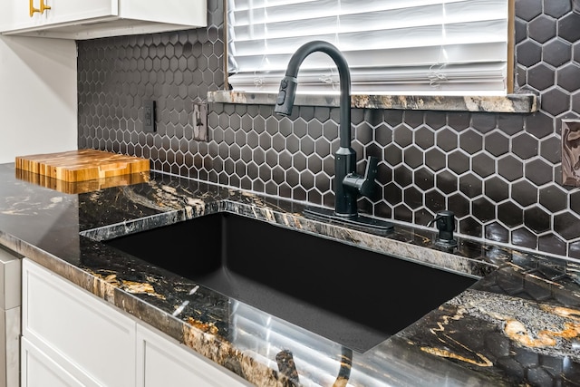 details featuring backsplash, dark stone counters, sink, and white cabinets