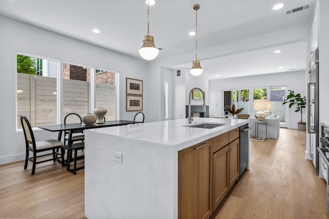 kitchen featuring sink, pendant lighting, a kitchen island with sink, and light hardwood / wood-style flooring