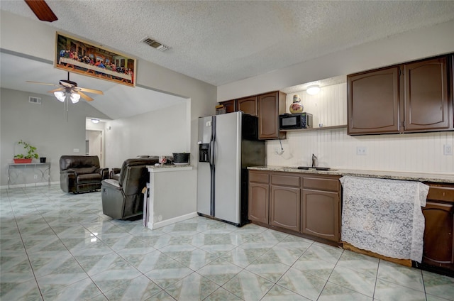 kitchen featuring dark brown cabinetry, sink, vaulted ceiling, a textured ceiling, and stainless steel fridge