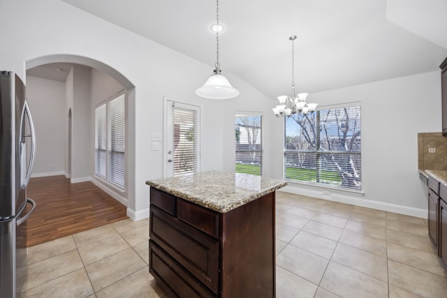 kitchen featuring dark brown cabinetry, light tile patterned floors, stainless steel refrigerator, pendant lighting, and light stone countertops