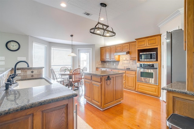 kitchen featuring a kitchen island, sink, hanging light fixtures, stainless steel appliances, and light hardwood / wood-style flooring