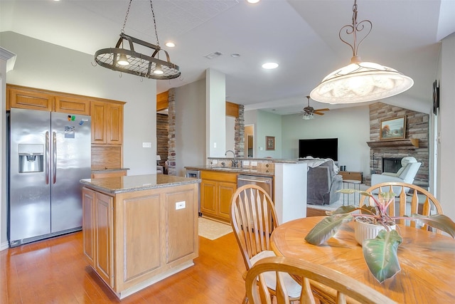 kitchen with stainless steel refrigerator with ice dispenser, a stone fireplace, light hardwood / wood-style floors, and kitchen peninsula