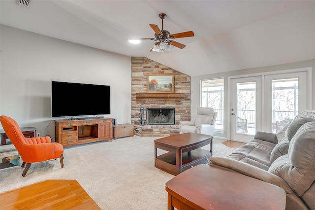 carpeted living room featuring a stone fireplace, vaulted ceiling, and ceiling fan