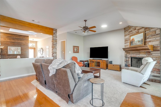 living room with vaulted ceiling with beams, a stone fireplace, ceiling fan with notable chandelier, and light wood-type flooring