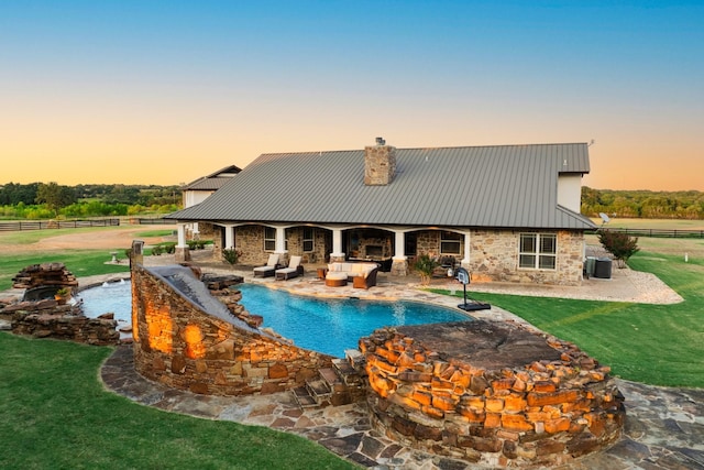 pool at dusk with a lawn, cooling unit, exterior fireplace, and a patio area