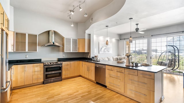 kitchen featuring light brown cabinetry, kitchen peninsula, pendant lighting, stainless steel appliances, and wall chimney range hood