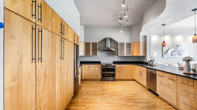 kitchen with wall chimney exhaust hood, hanging light fixtures, light brown cabinets, appliances with stainless steel finishes, and light hardwood / wood-style floors