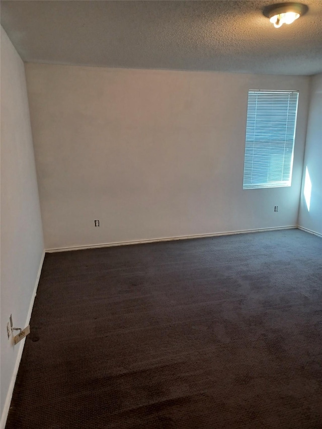 spare room with a textured ceiling and dark carpet