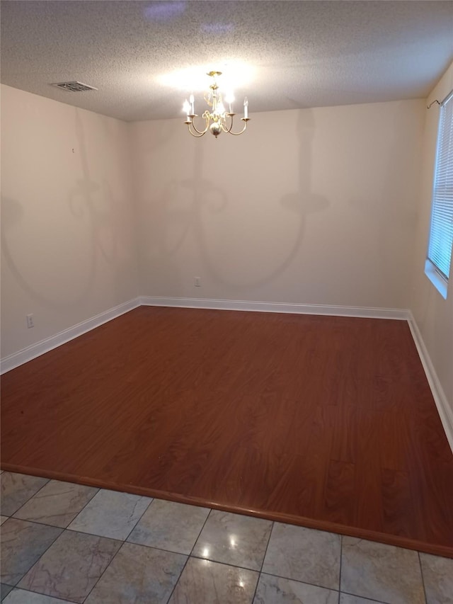 spare room with an inviting chandelier, hardwood / wood-style floors, and a textured ceiling