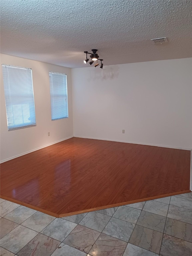 empty room with light wood-type flooring and a textured ceiling