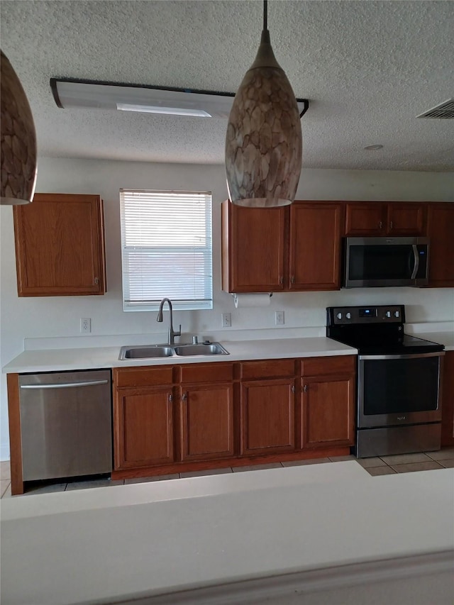 kitchen with appliances with stainless steel finishes, sink, hanging light fixtures, and a textured ceiling