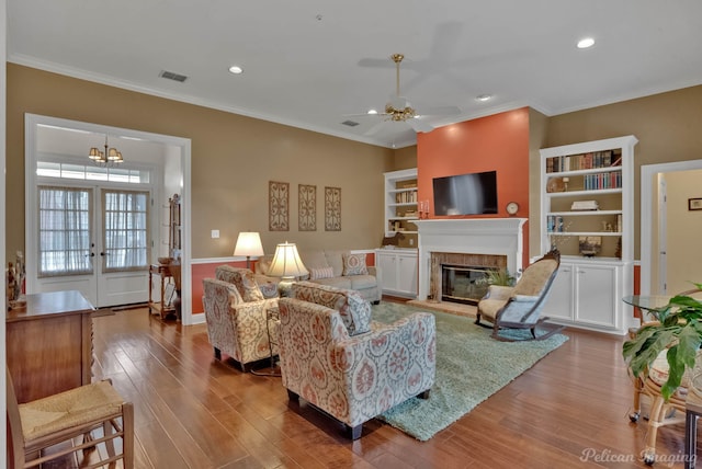 living room with ceiling fan with notable chandelier, ornamental molding, and light hardwood / wood-style floors