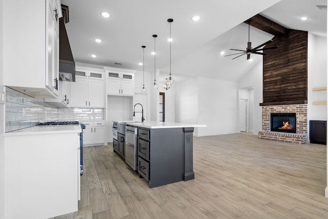 kitchen featuring white cabinetry, a kitchen island with sink, a fireplace, decorative light fixtures, and stainless steel dishwasher