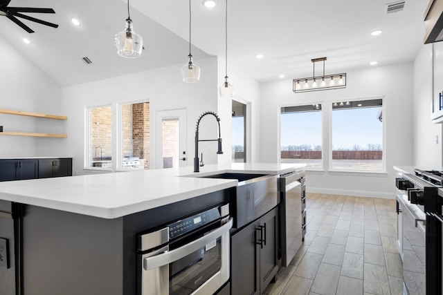 kitchen with hanging light fixtures, stainless steel oven, stove, and a center island with sink