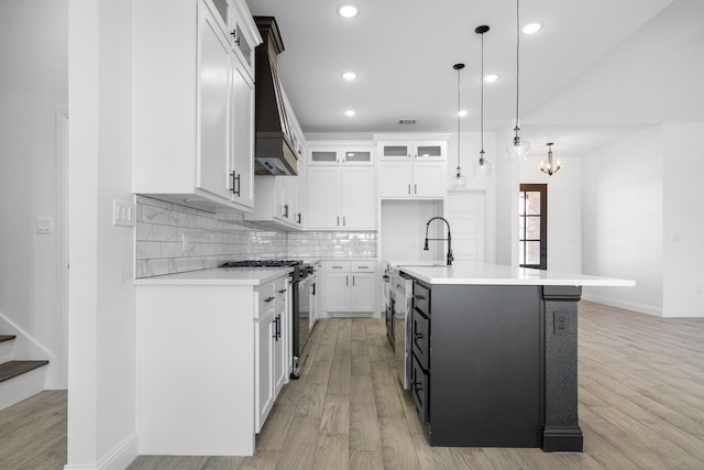 kitchen featuring sink, stainless steel gas stove, an island with sink, pendant lighting, and white cabinets