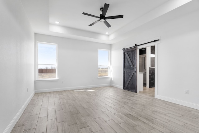 unfurnished bedroom featuring a raised ceiling, ceiling fan, a barn door, and light wood-type flooring