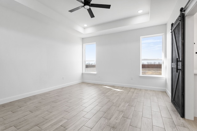 unfurnished room with ceiling fan, a barn door, a raised ceiling, and light hardwood / wood-style flooring