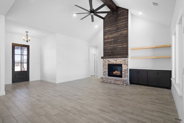 unfurnished living room with beamed ceiling, wood-type flooring, a brick fireplace, and ceiling fan with notable chandelier