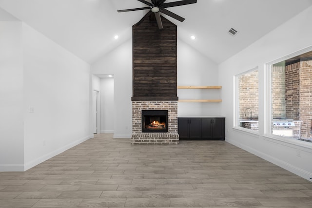 unfurnished living room with a brick fireplace, high vaulted ceiling, ceiling fan, and light wood-type flooring