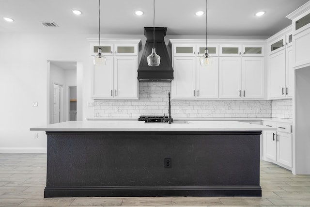 kitchen with pendant lighting, custom exhaust hood, white cabinets, and a center island with sink