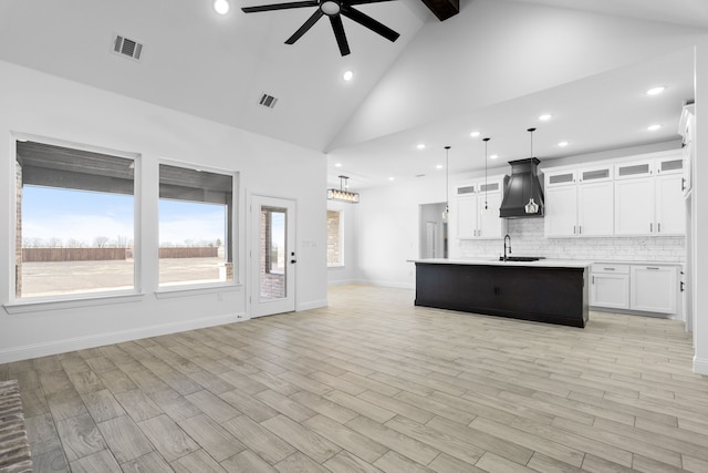 kitchen with hanging light fixtures, an island with sink, light hardwood / wood-style floors, decorative backsplash, and white cabinets