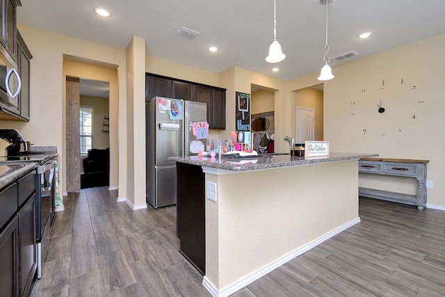 kitchen with an island with sink, appliances with stainless steel finishes, dark brown cabinets, and decorative light fixtures