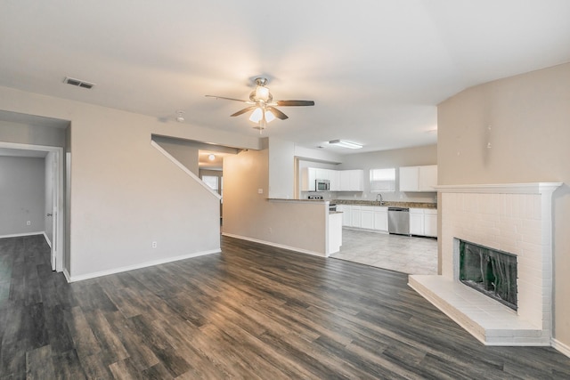 unfurnished living room with a brick fireplace, wood-type flooring, sink, and ceiling fan